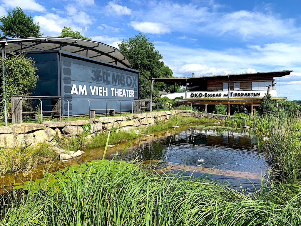 A view of a small pond, with a restaurant "Öko-Essbar" seen in the background.